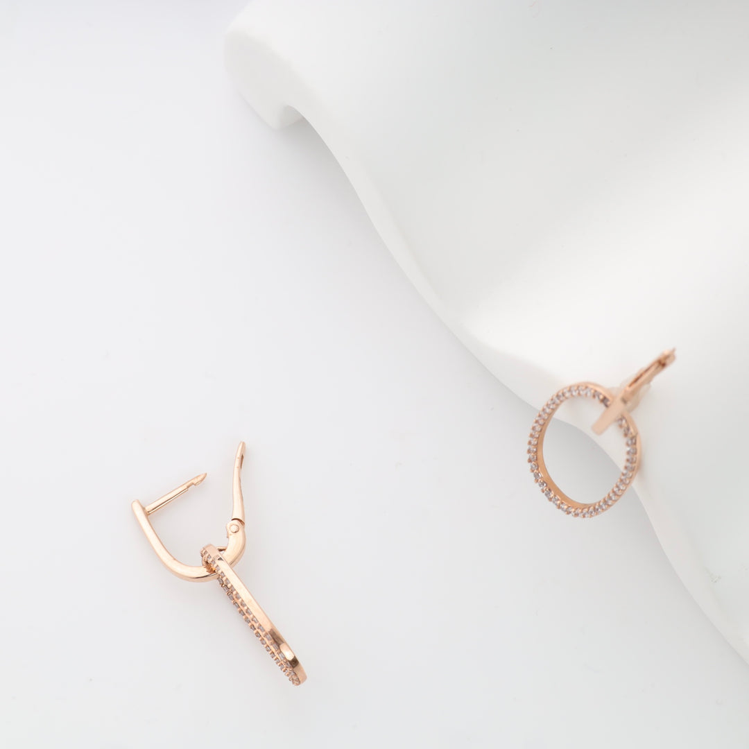 Rose gold hoop earrings with small embedded stones shown on a white surface.