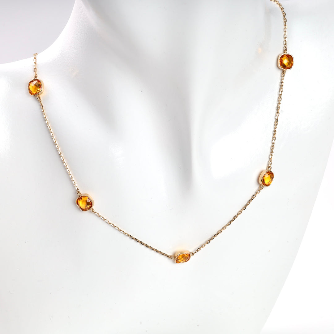 Gold chain necklace with four faceted amber stones displayed on a white mannequin bust.
