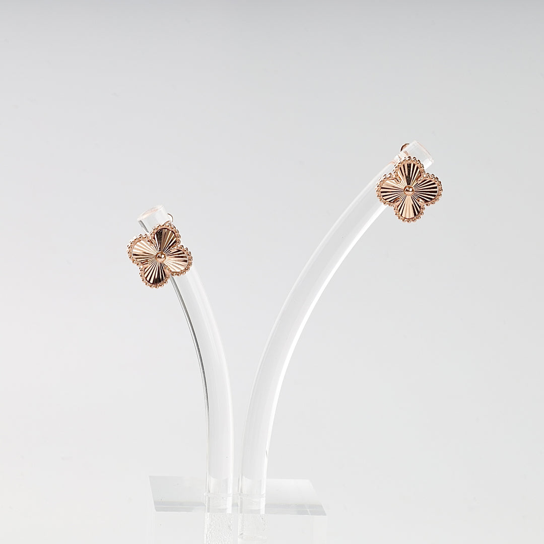 Pair of gold floral earrings on a clear stand against a light gray background