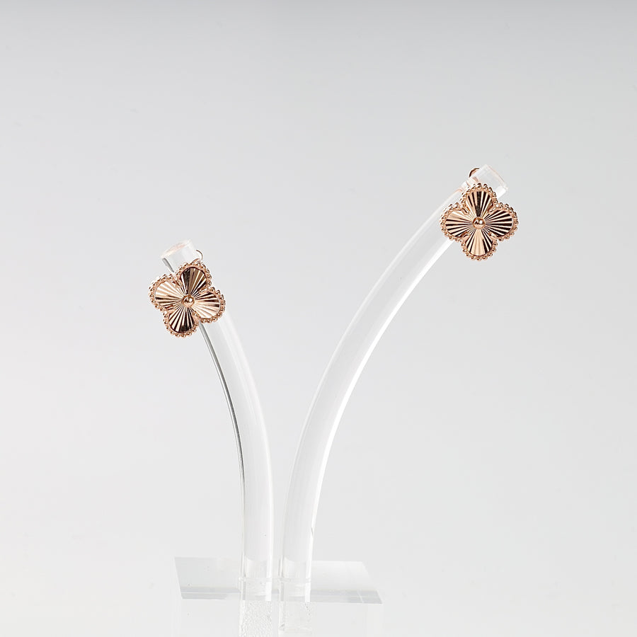 Pair of gold floral earrings on a clear stand against a light gray background