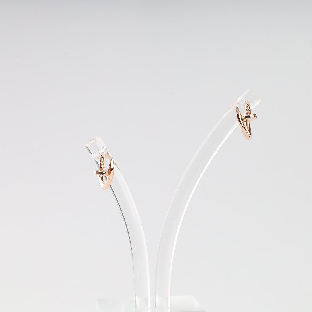 Pair of rose gold knot hoop earrings displayed on a clear stand against a white background.