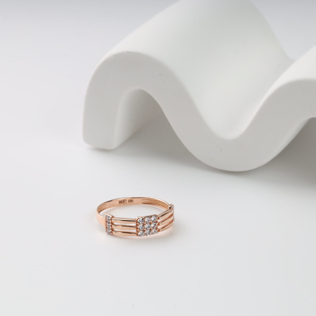 Rose gold diamond ring with multiple bands displayed on a white wavy background.