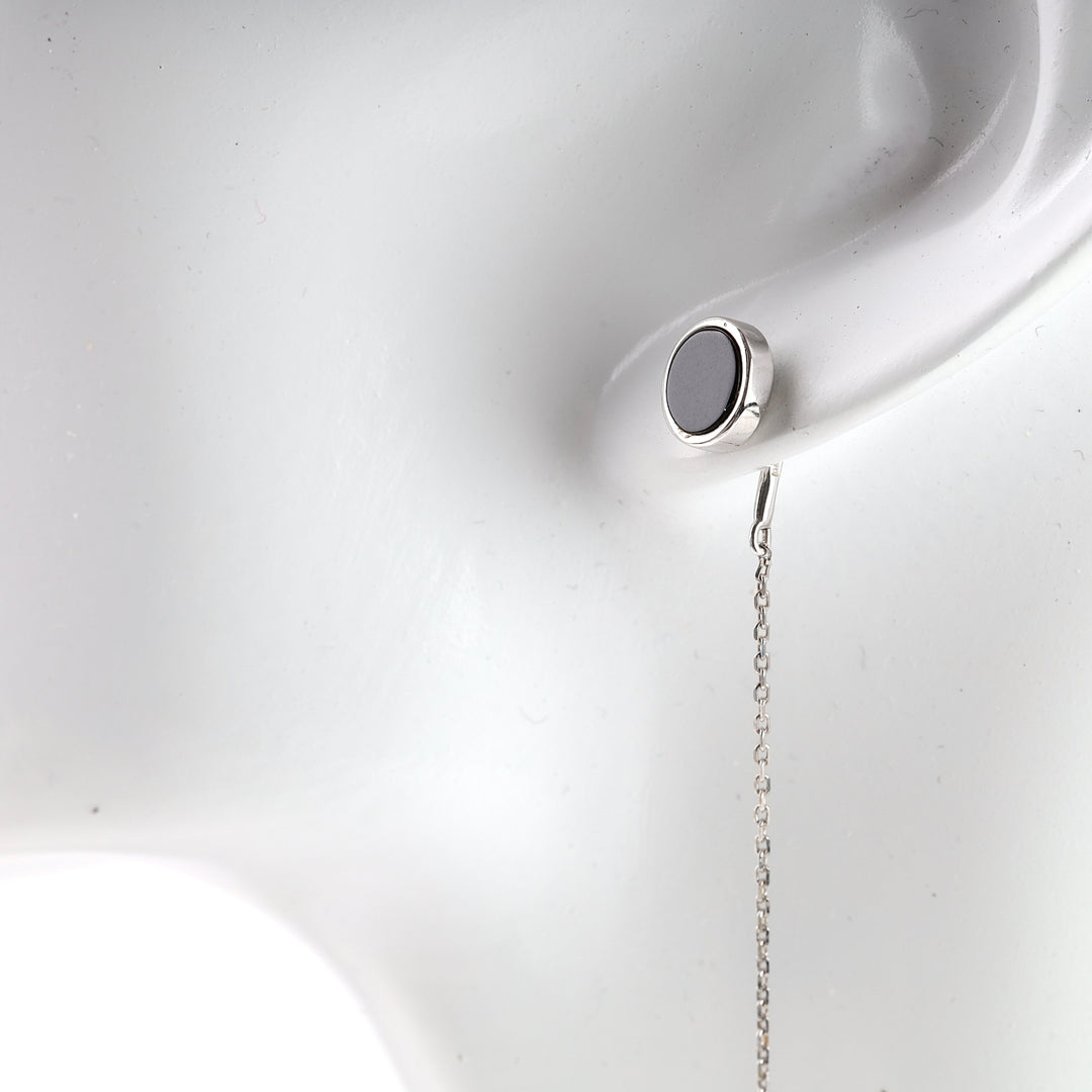 Single silver stud earring with a black circle and a delicate chain, displayed on a white mannequin ear.