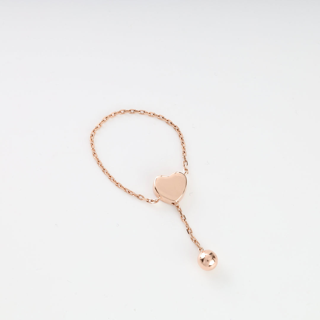 Rose gold chain ring with a heart charm and dangling ball displayed on a white background.