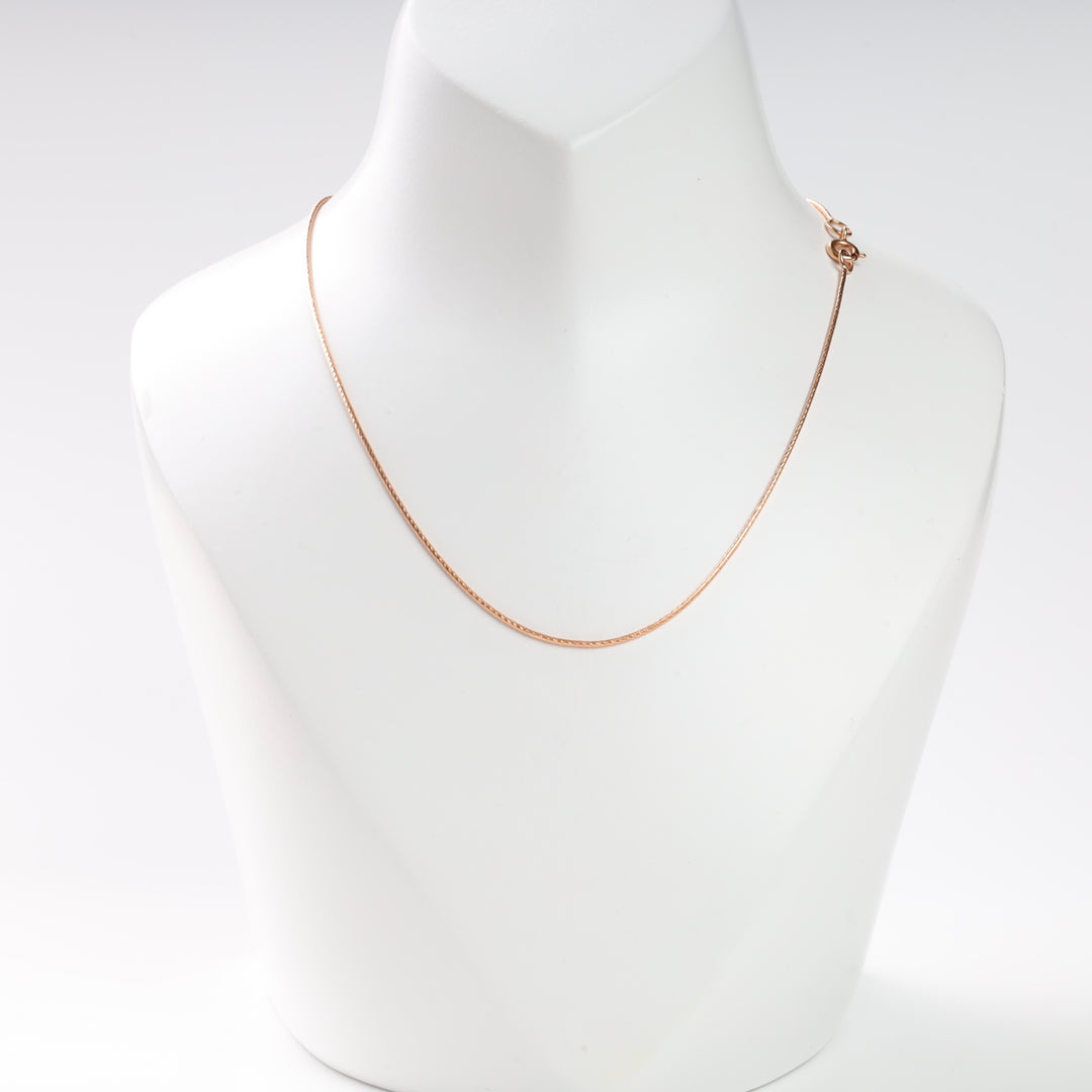 A rose gold chain necklace displayed on a white mannequin.
