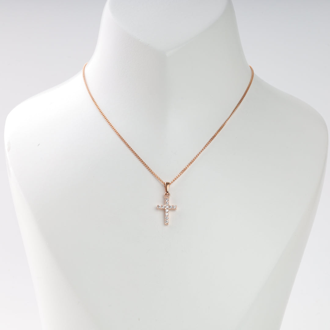 Rose gold necklace with a small cross pendant set with clear stones, displayed on a white bust. Cross necklace jewelry.