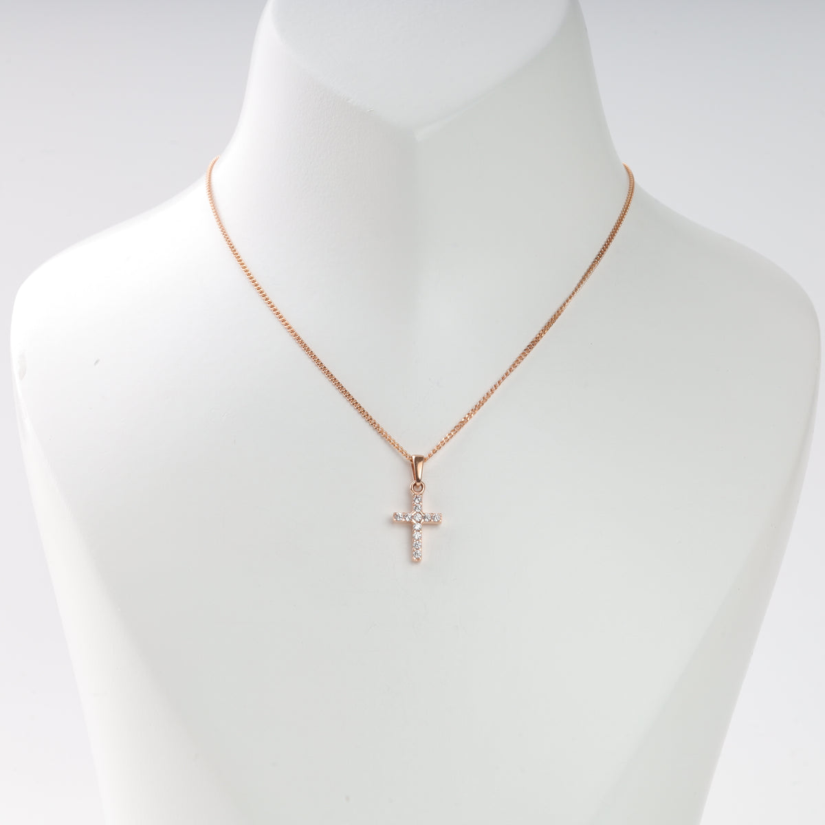 Rose gold necklace with a small cross pendant set with clear stones, displayed on a white bust. Cross necklace jewelry.