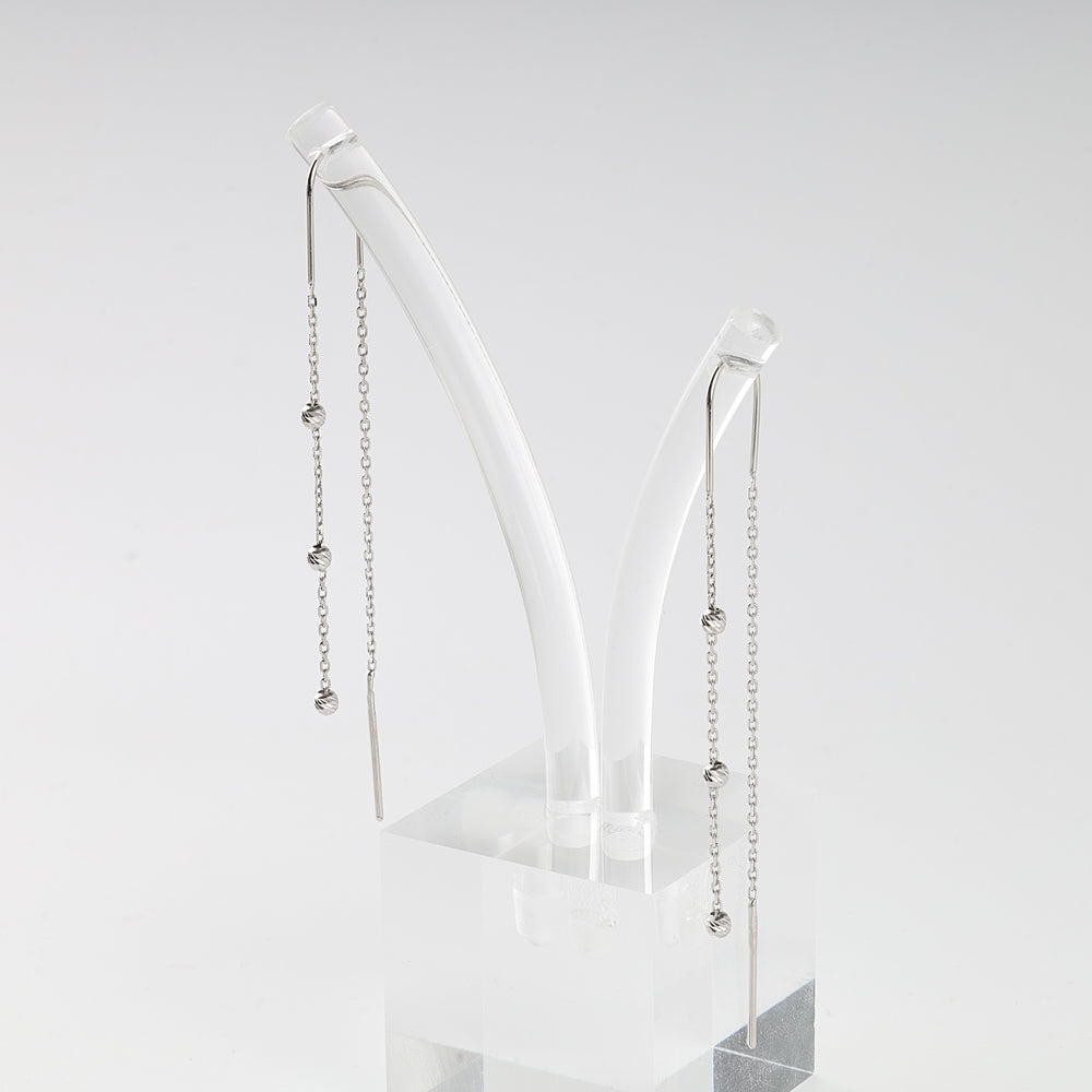 Pair of silver threader earrings with small knot beads on delicate chains displayed on a clear acrylic stand.
