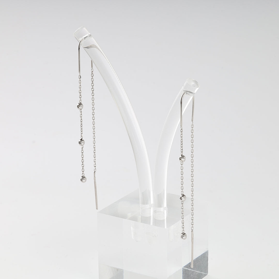 Pair of silver threader earrings with small knot beads on delicate chains displayed on a clear acrylic stand.