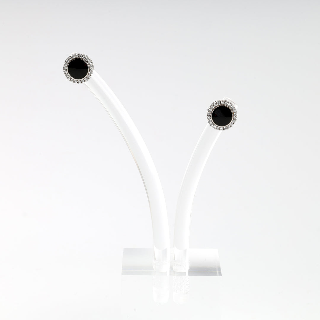 Pair of round black onyx stud earrings with clear gem halos, set in silver, displayed on a white stand.