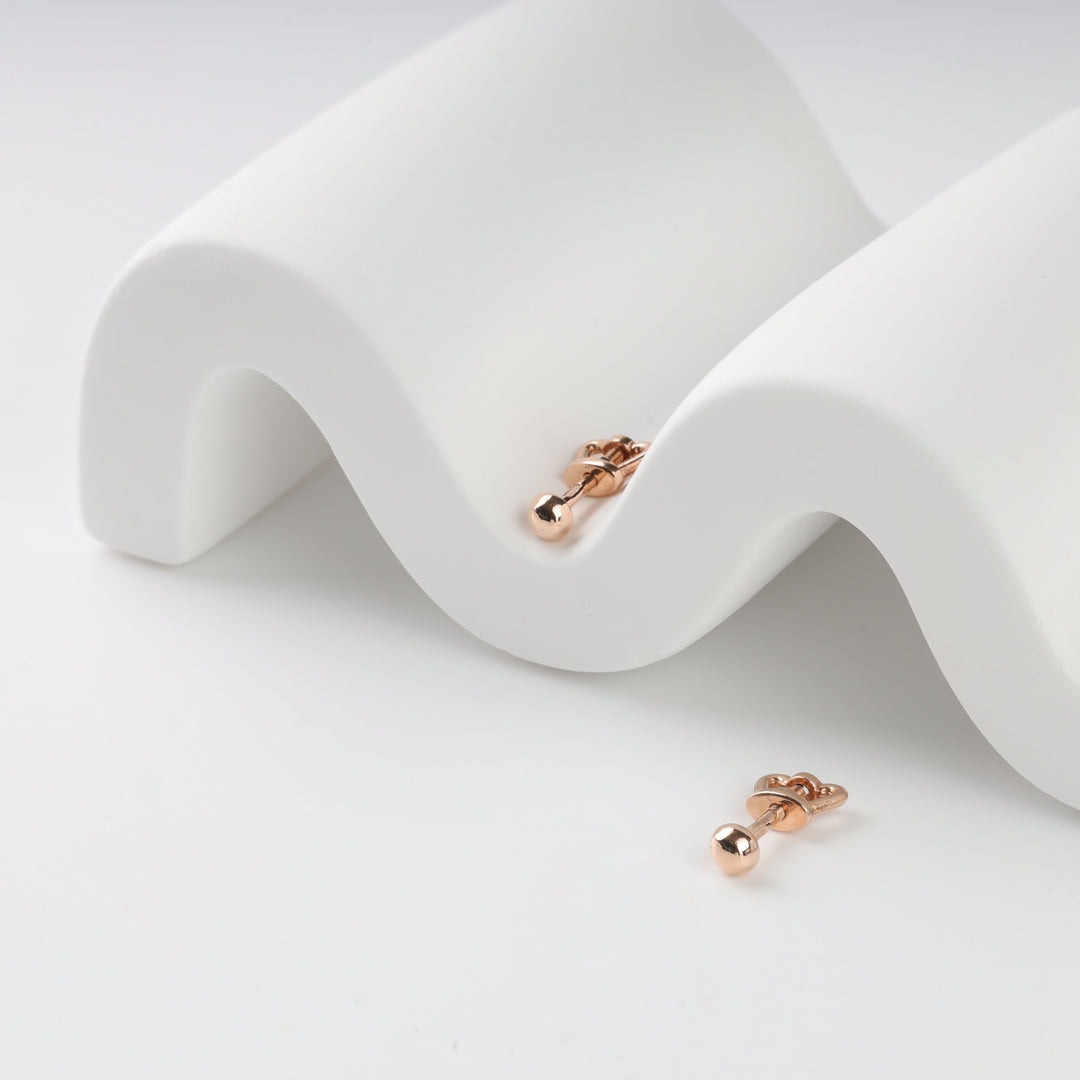 Gold barbell earrings displayed on a white wavy stand.
