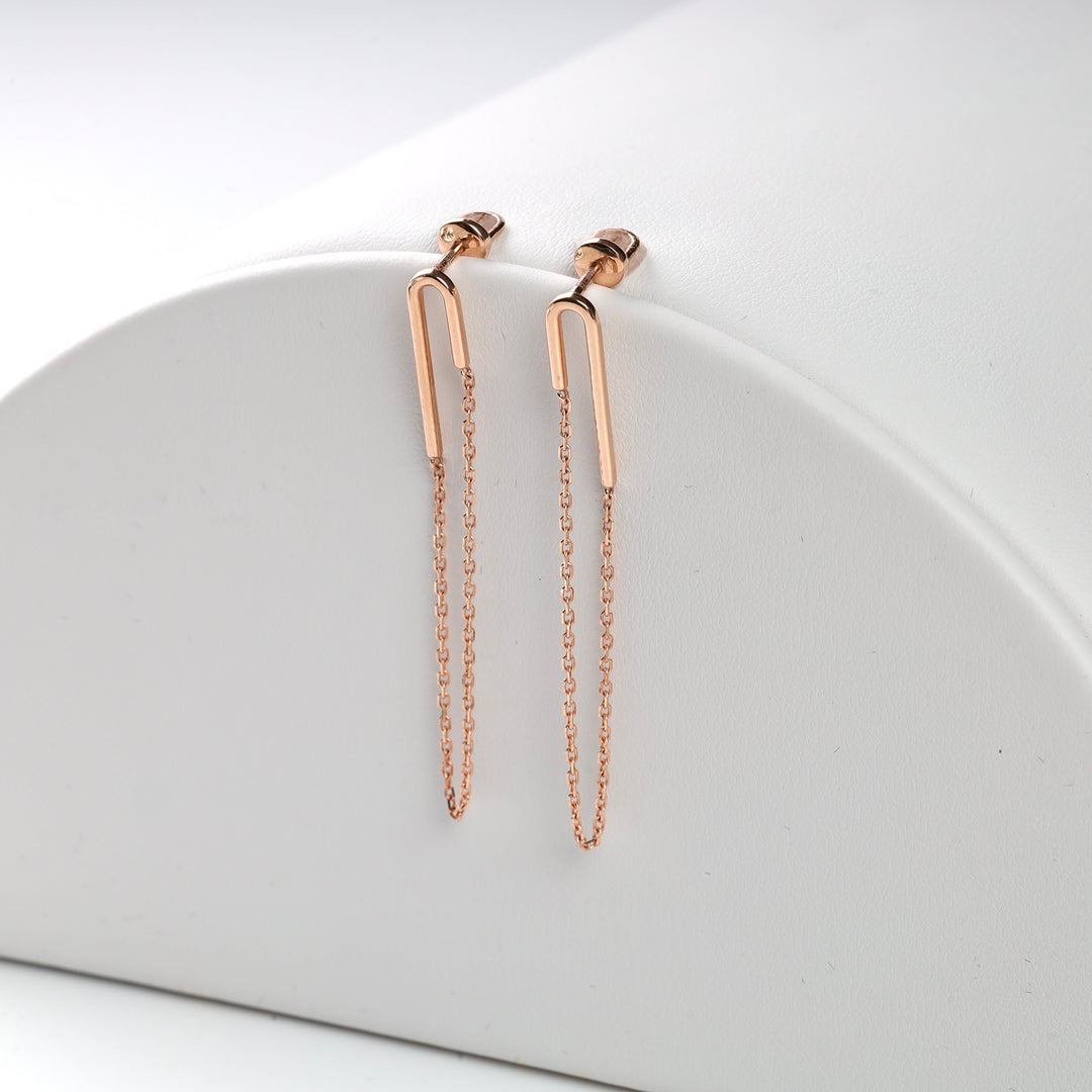 Rose gold chain earrings with geometric hooks on white background. Minimalist jewelry, dangle earrings, fashion accessories.