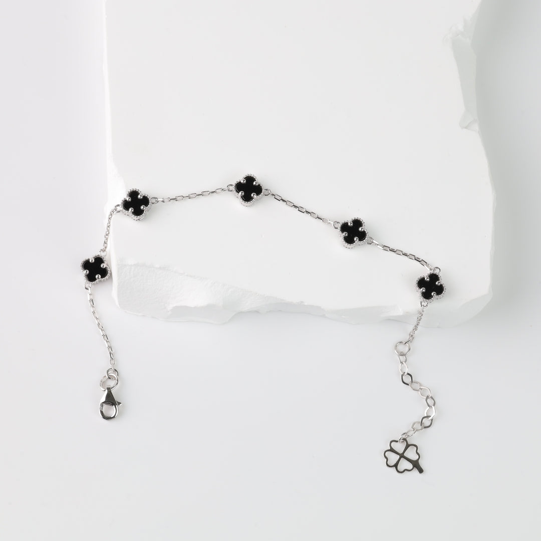 Silver chain bracelet with five black enamel four-leaf clover charms displayed on a white background.