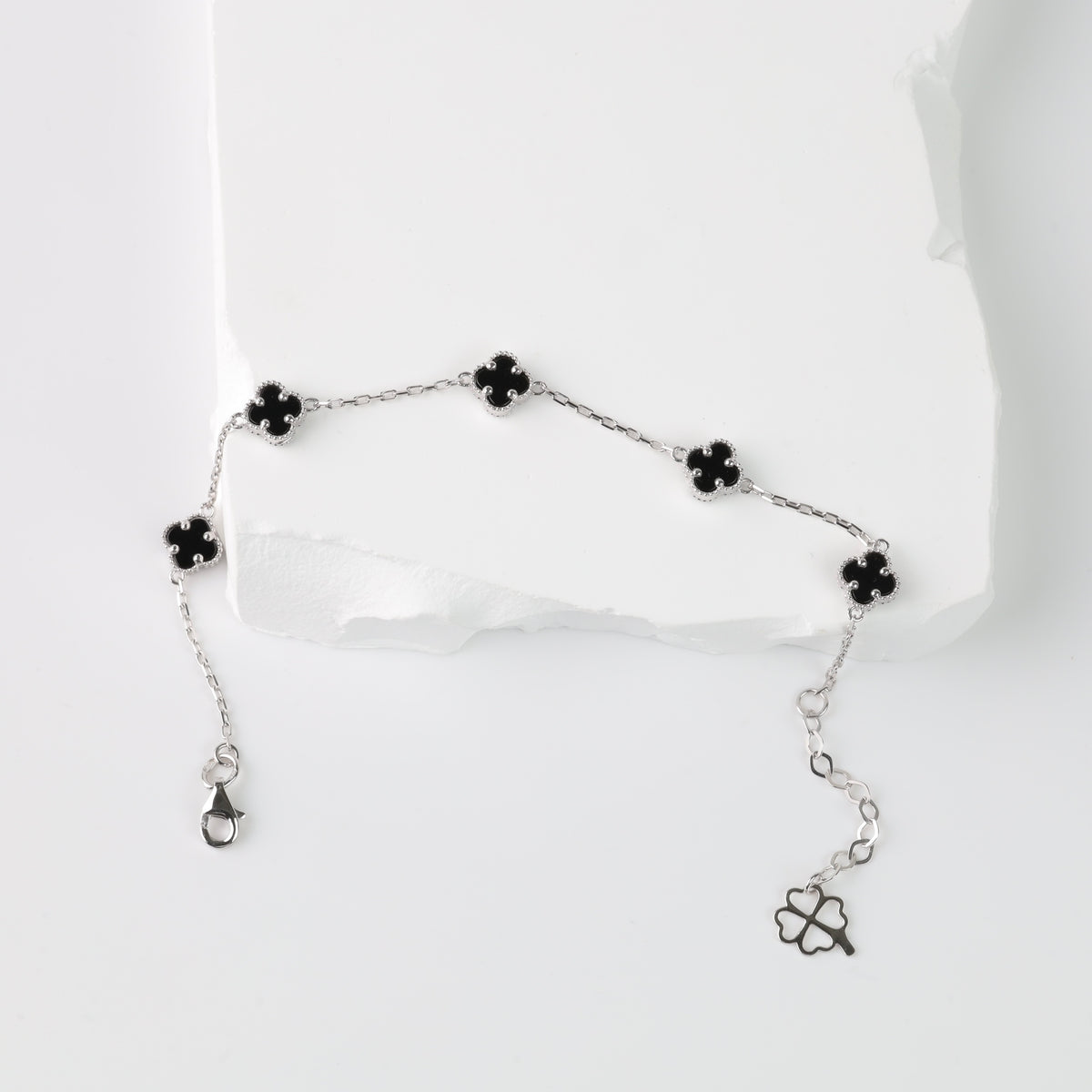 Silver chain bracelet with five black enamel four-leaf clover charms displayed on a white background.