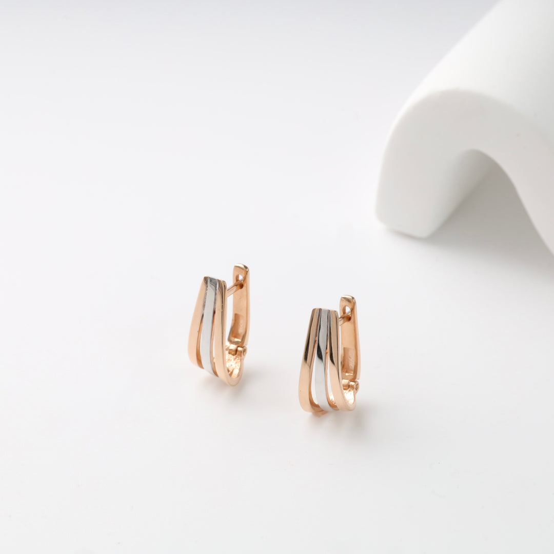 Two-tone rose and silver huggie earrings on a white surface.