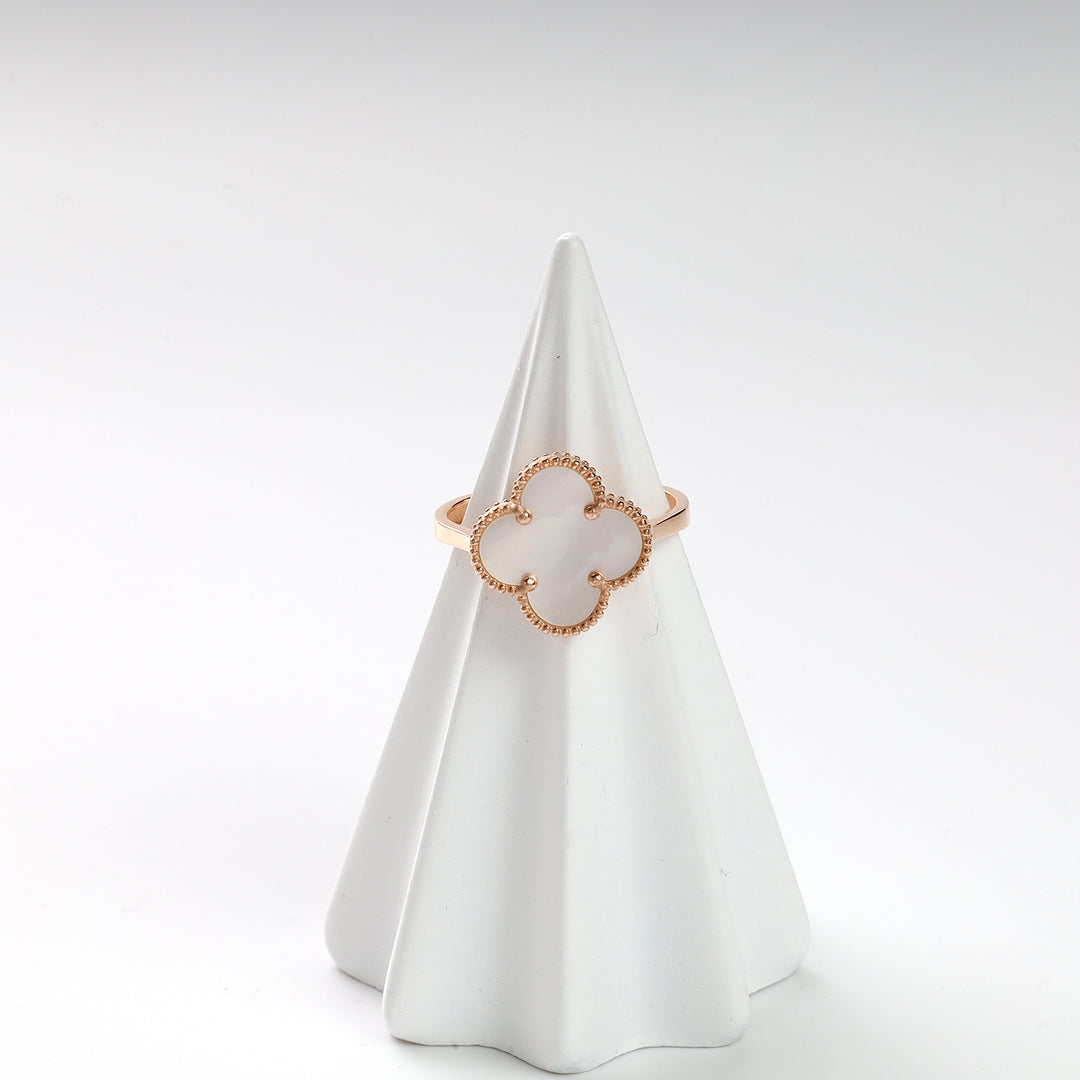 Gold clover motif ring with white inlay displayed on a white ring cone, fine jewelry, geometric ring, minimalist style.