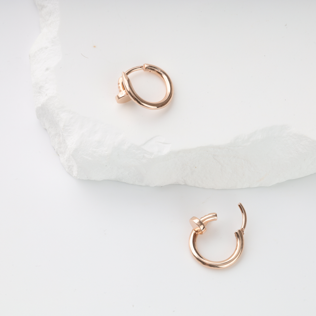 Pair of rose gold hoop earrings with hexagon screw motif displayed on white textured stone background.