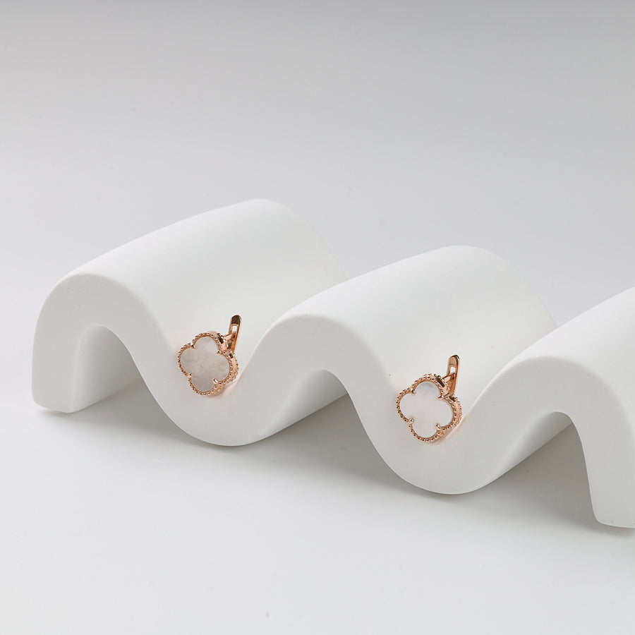Rose gold clover earrings with white enamel accents displayed on a white wavy stand.