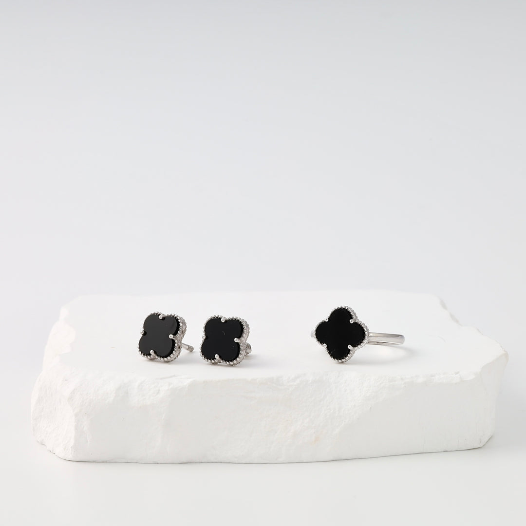 Sterling silver black clover stud earrings and matching ring set displayed on white stone, Ukrainian Jewelry, black onyx jewelry.
