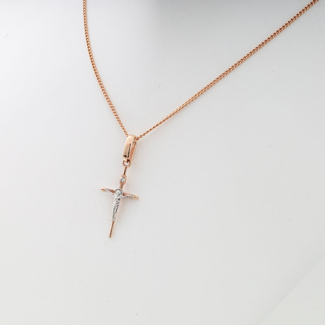 Rose gold chain necklace with a small crucifix pendant featuring silver accents, shown on a white display stand.