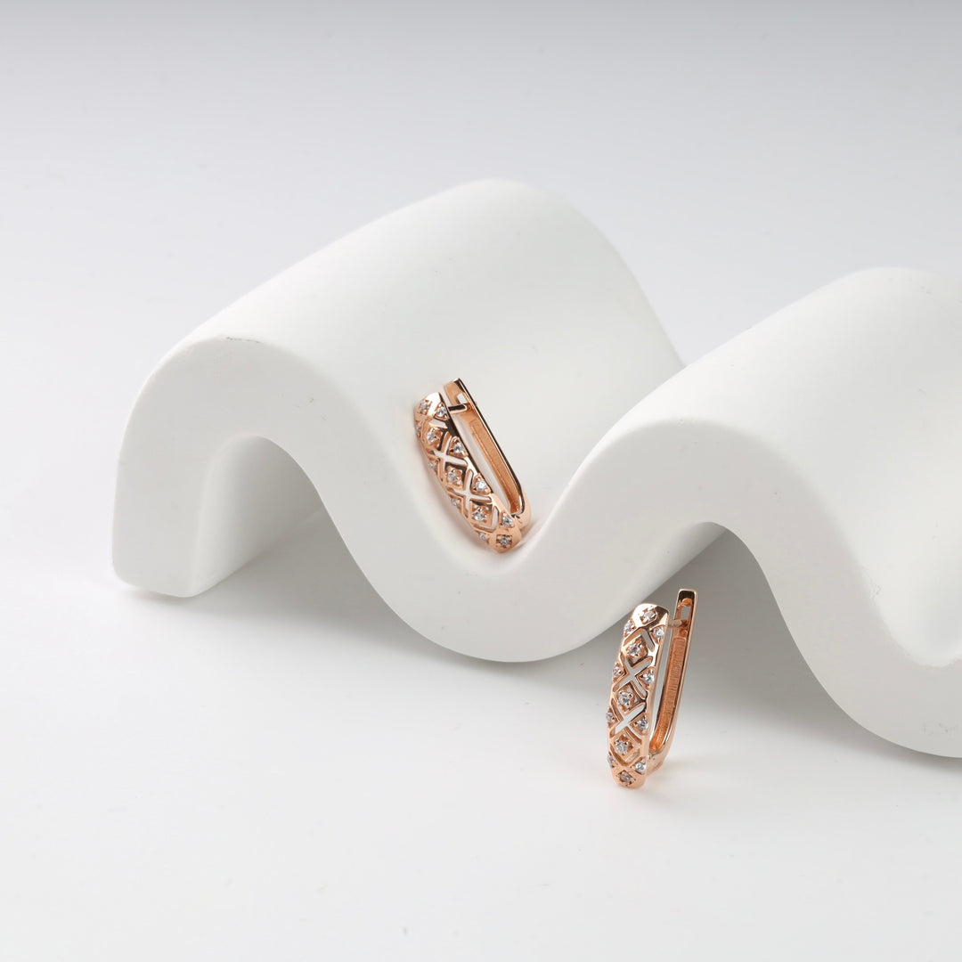 Rose gold diamond huggie earrings with lattice design on white wavy display.
