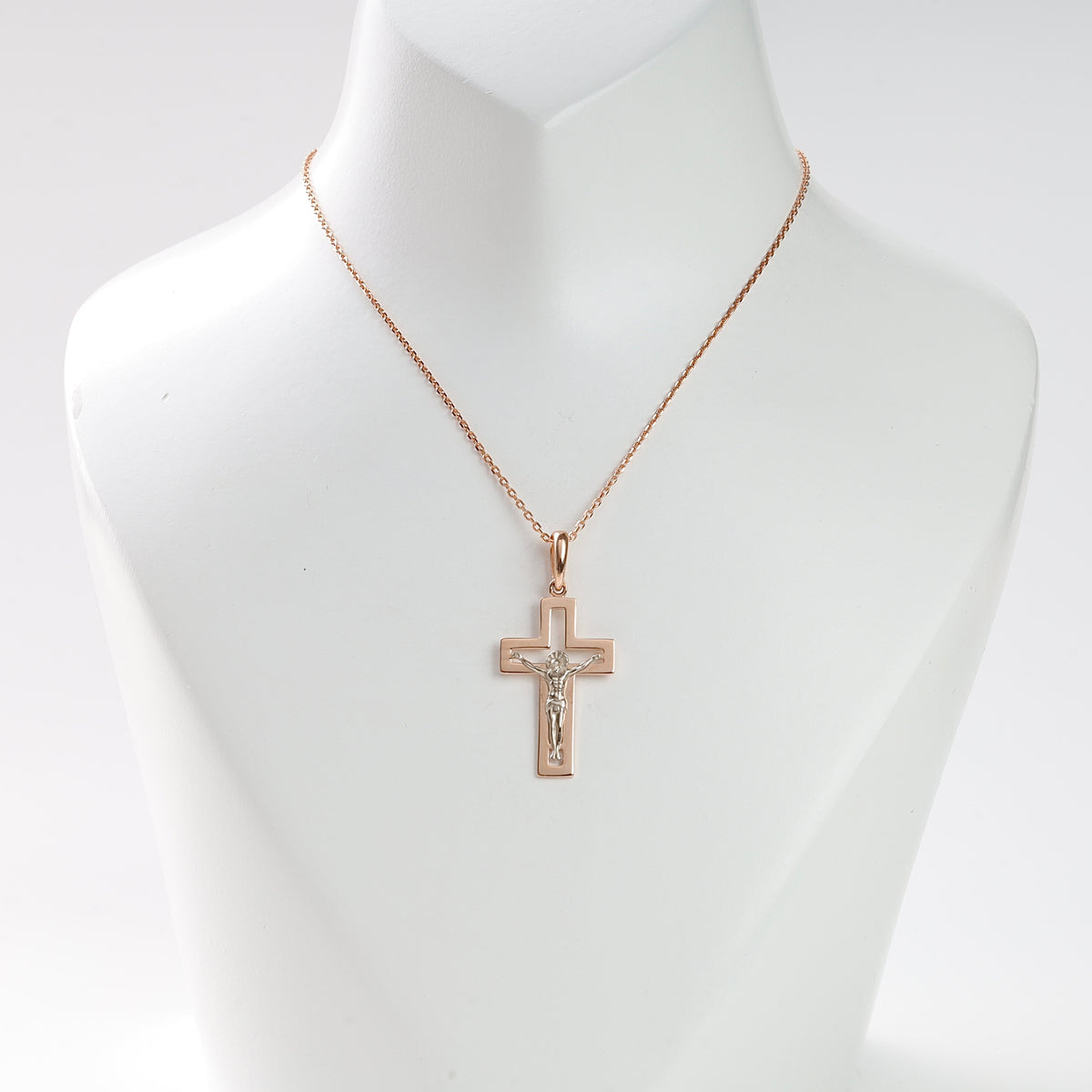 Rose gold crucifix pendant necklace with a silver Jesus motif displayed on a white jewelry bust.
