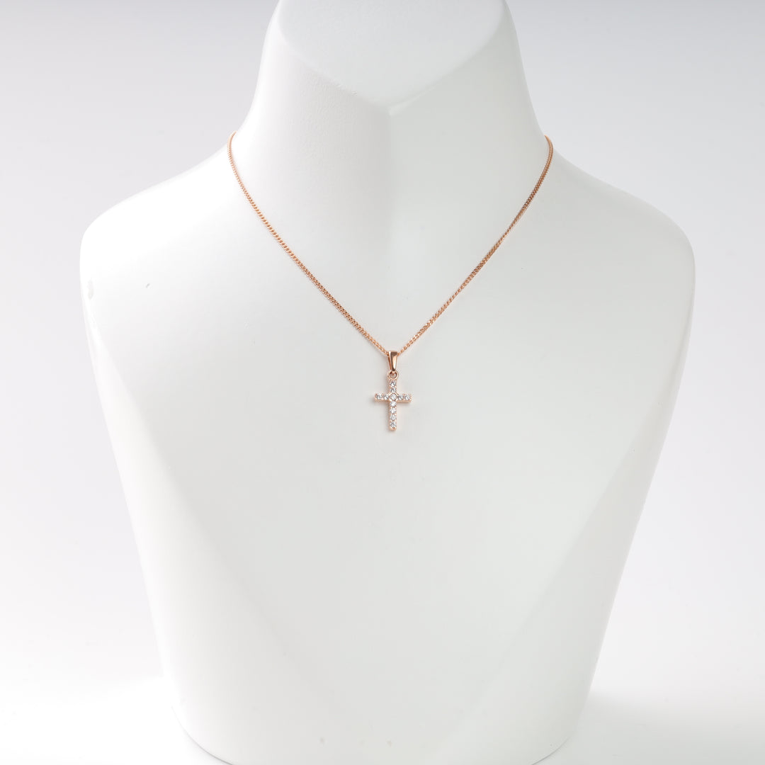 Rose gold chain necklace with a small cross pendant adorned with clear stones, displayed on a white necklace stand.
