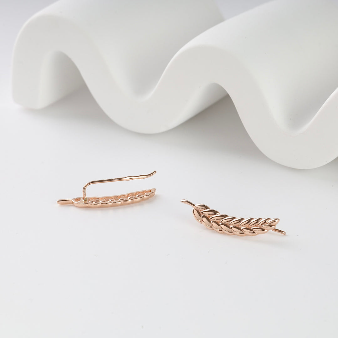 Pair of rose gold leaf ear climber earrings displayed on a white surface, jewelry, leaf motif, ear crawler.