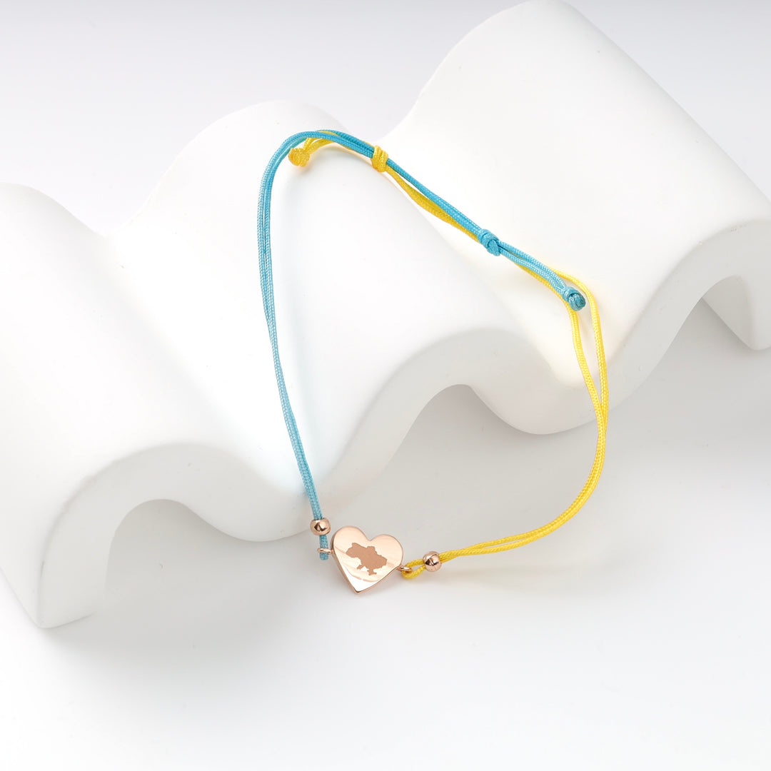 Gold heart charm bracelet with blue and yellow cord on white wavy display.