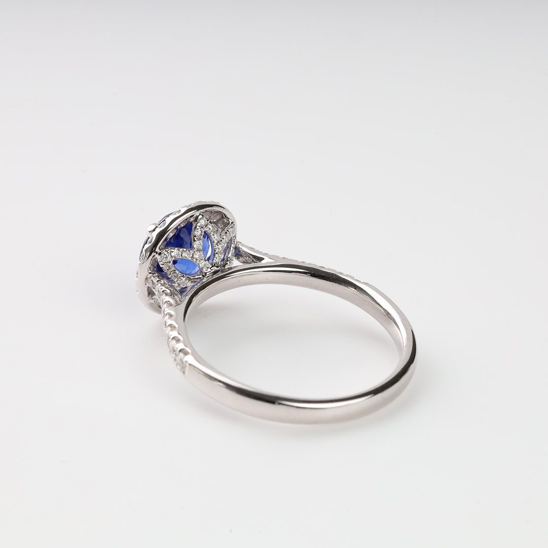 Silver engagement ring with blue gemstone and intricate filigree setting on white background, fine jewelry ring.