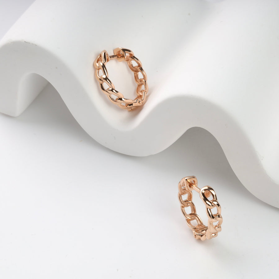 Rose gold chain link hoop earrings on a white wavy display.