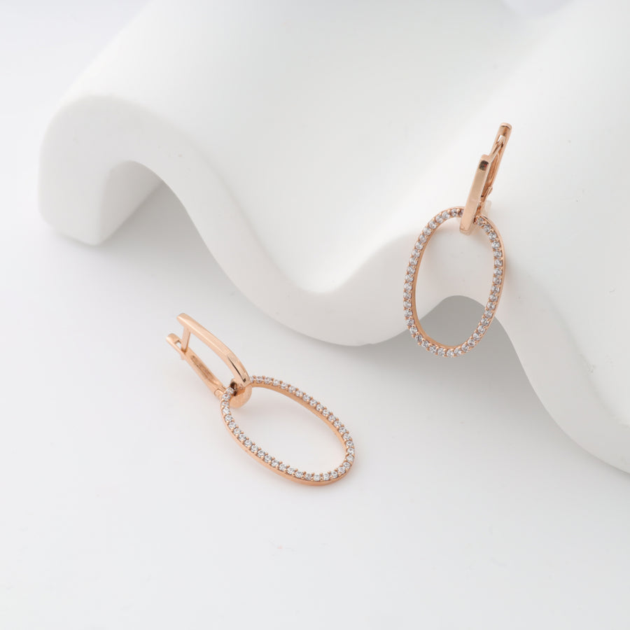 Rose gold oval hoop earrings with pave diamonds displayed on a white surface.