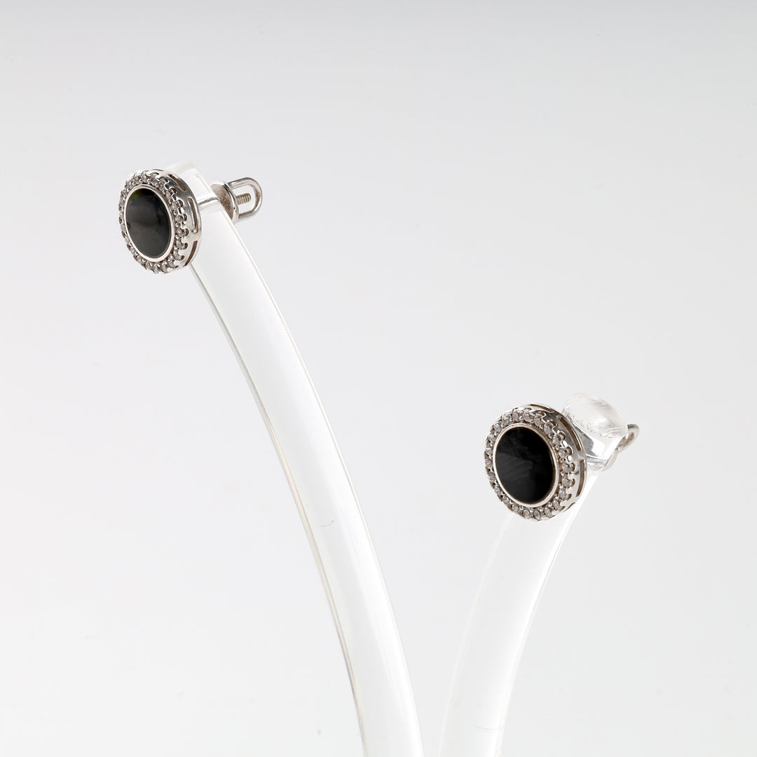 Pair of round silver stud earrings with black stone center and clear stone halo on a white display.