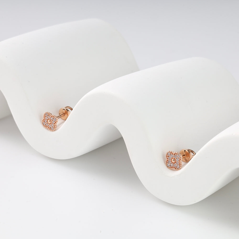 Square rose gold stud earrings with clear crystal pavé, displayed on a white wavy stand, minimalist jewelry.