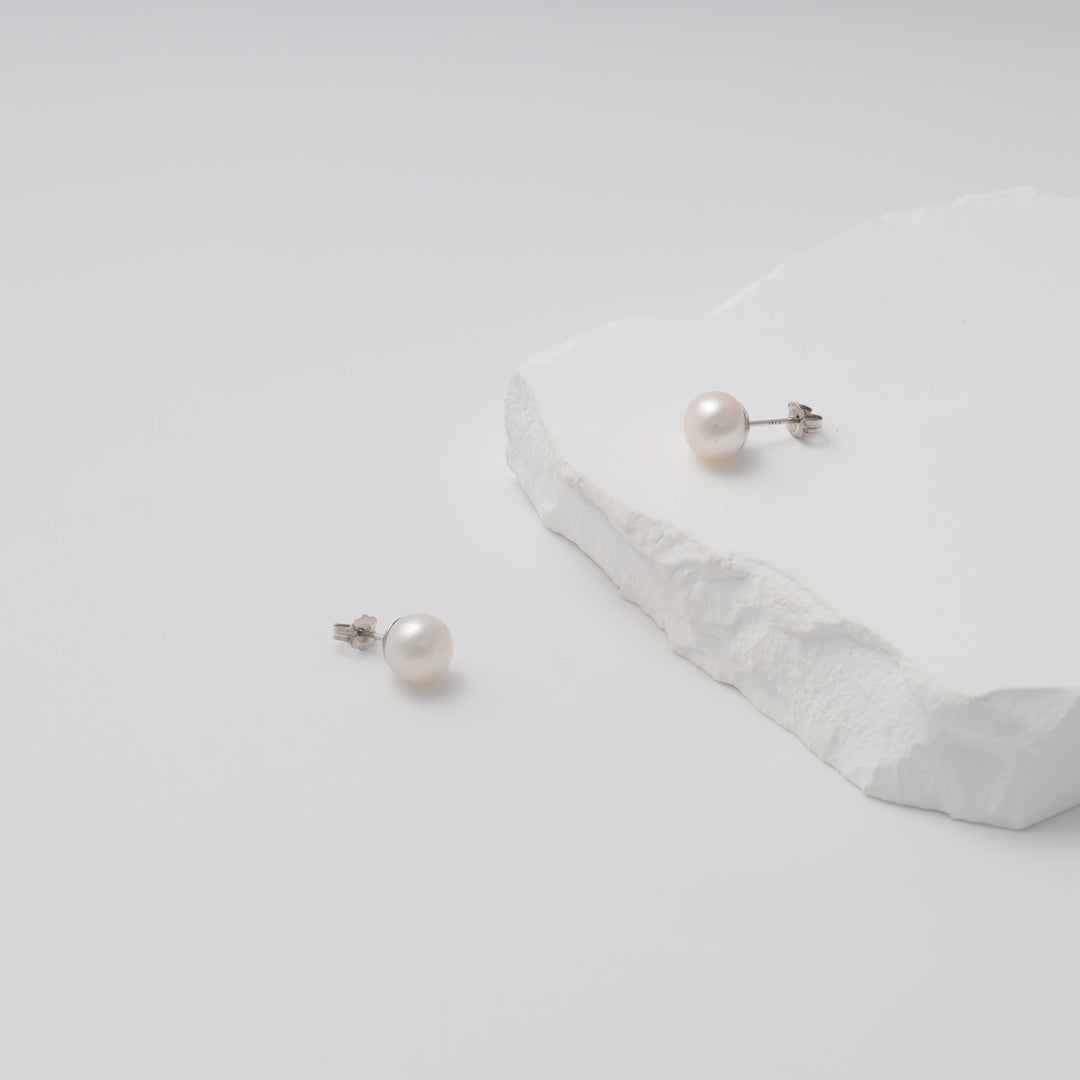 Sterling silver pearl stud earrings on white stone display, classic Ukrainian Jewelry for minimalist silver earrings shoppers.