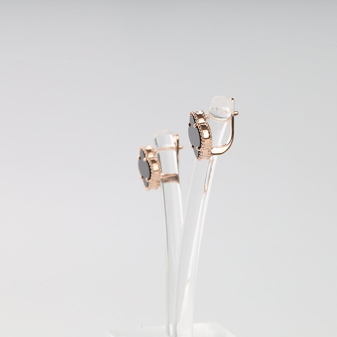 Pair of gold clip-on earrings with black oval stones displayed on a clear stand.