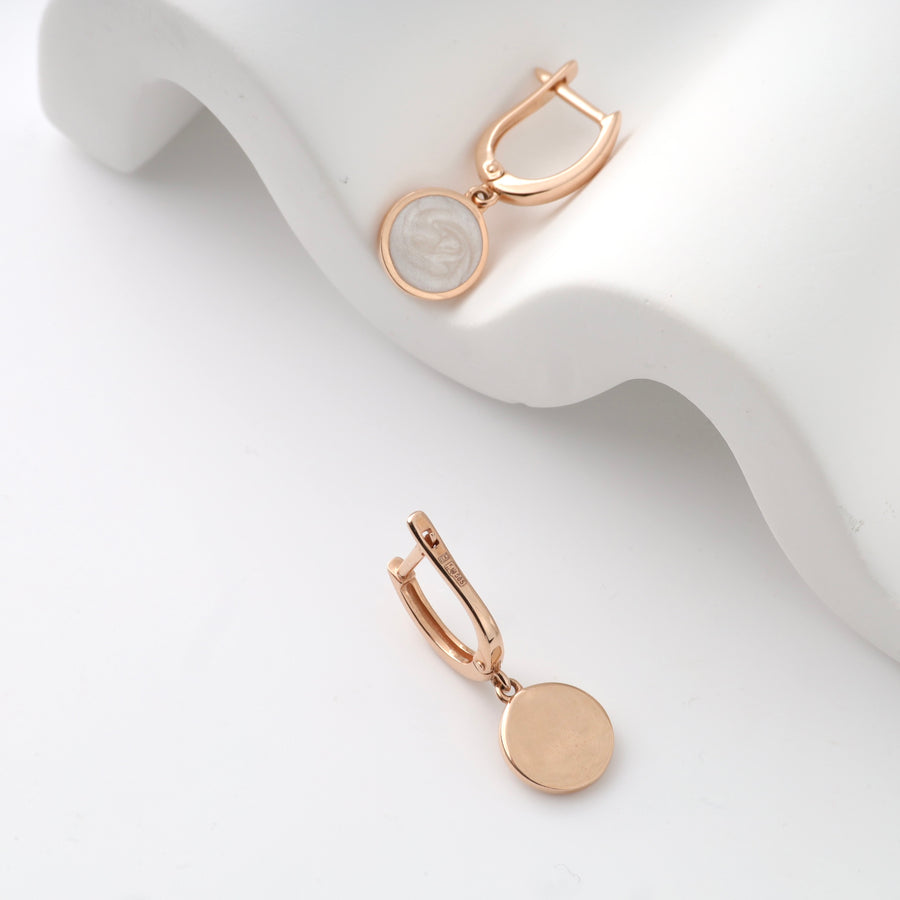 Rose gold drop earrings with round pendant on a white background.