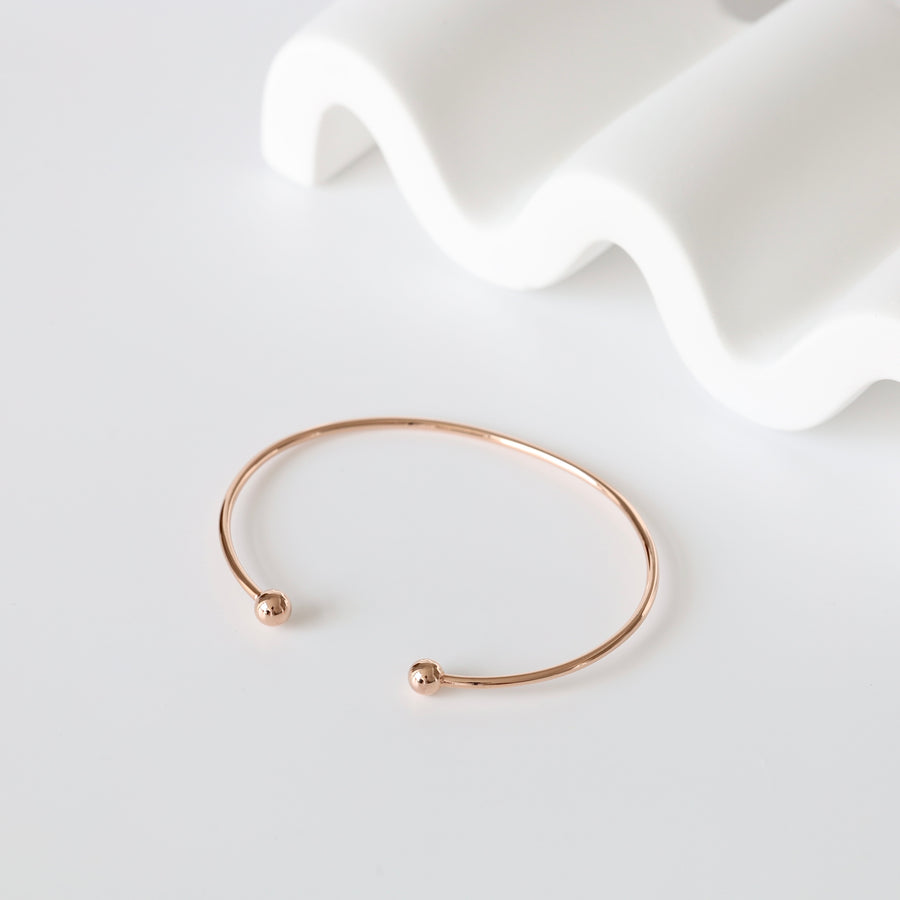 Simple rose gold open cuff bangle with rounded ends displayed on a white background, minimalist bracelet jewelry.