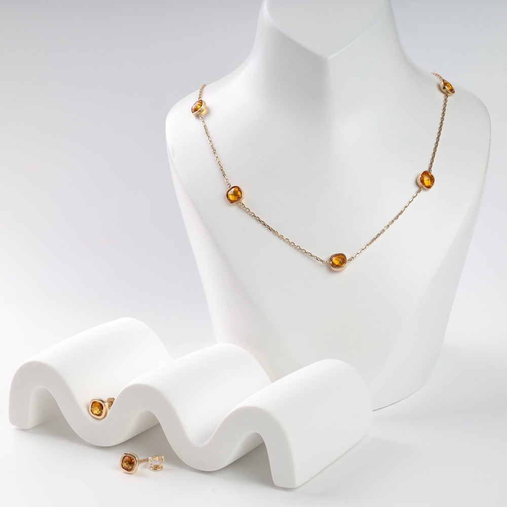 Gold necklace with amber gemstones displayed on white mannequin, accompanied by matching stud earrings.