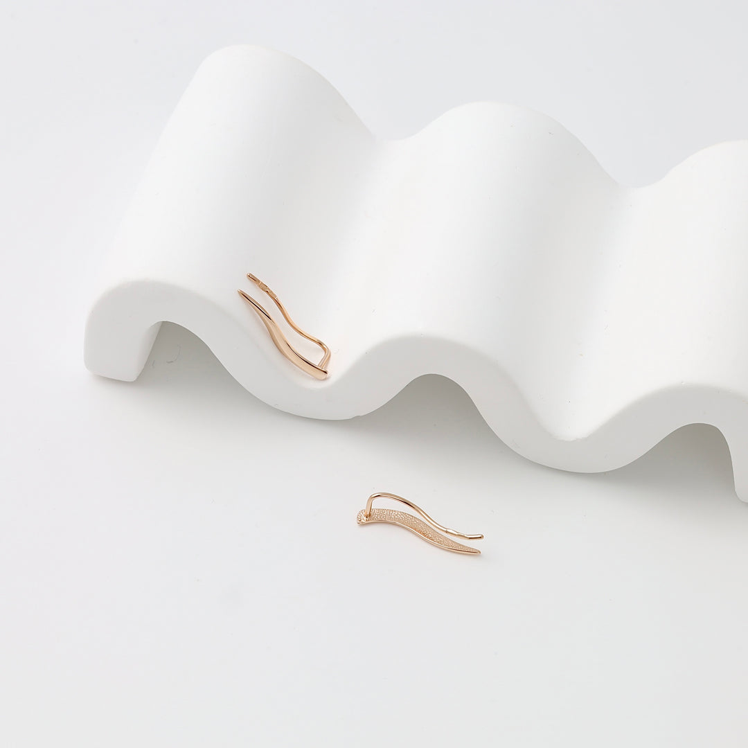 14k gold ear climber earrings with wave design and tiny crystals, displayed on white ceramic, modern Ukrainian Jewelry for women.