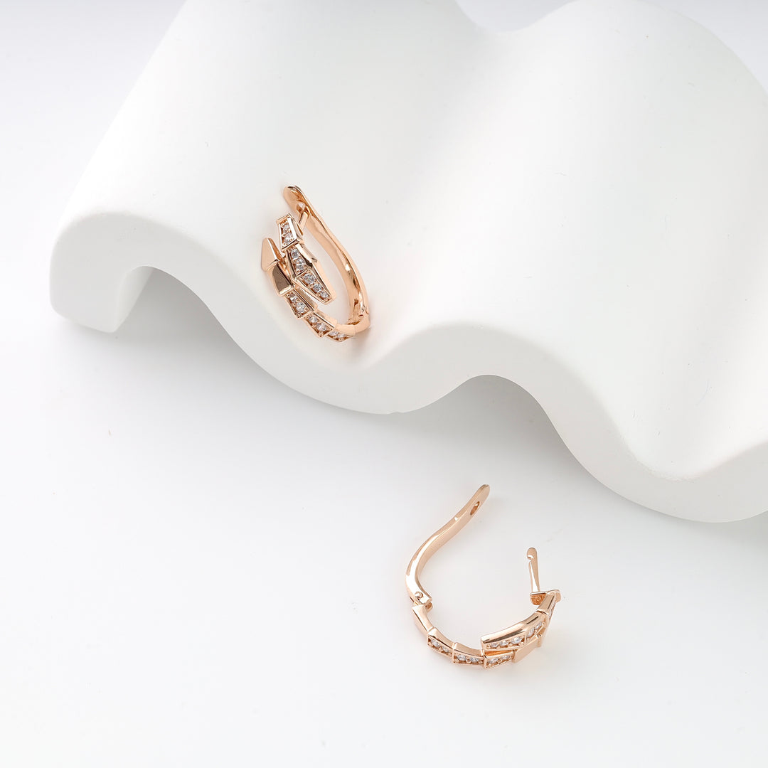 Pair of rose gold hoop earrings with clear cubic zirconia inlay, displayed on a white wavy ceramic stand.
