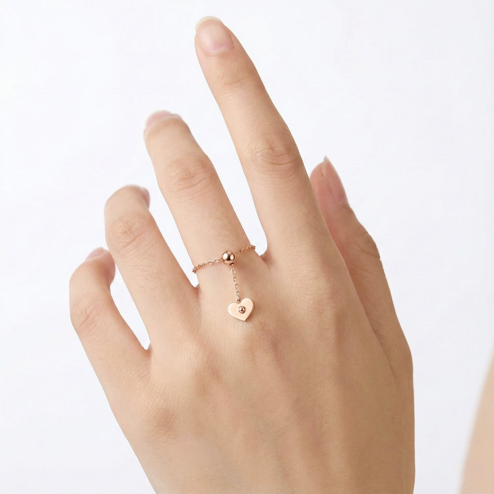 Hand wearing a rose gold ring with a heart charm on a white background