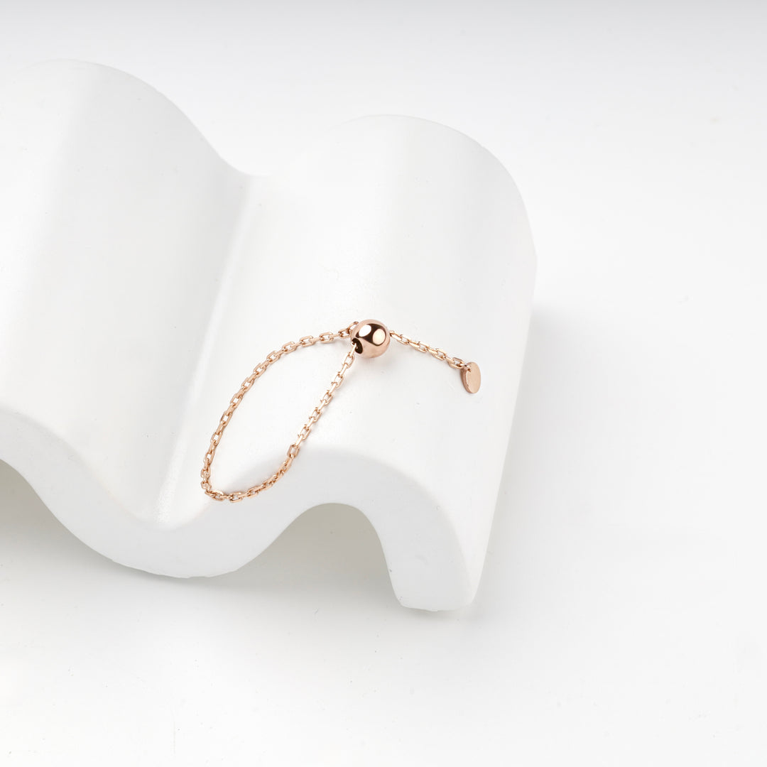 Rose gold ball chain ring resting on a white wave-shaped stand