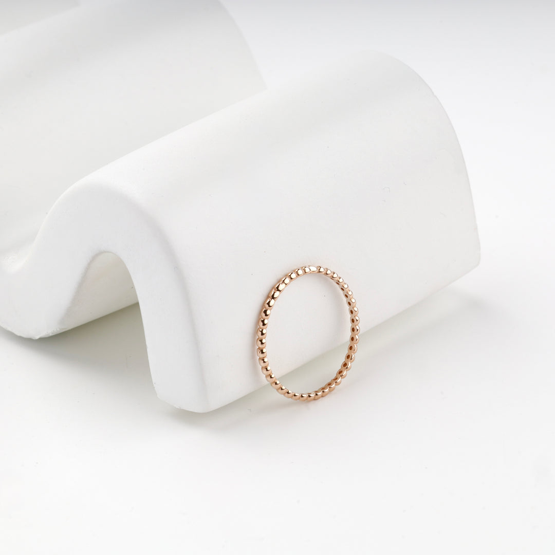 Rose gold beaded band ring standing against a white curved display