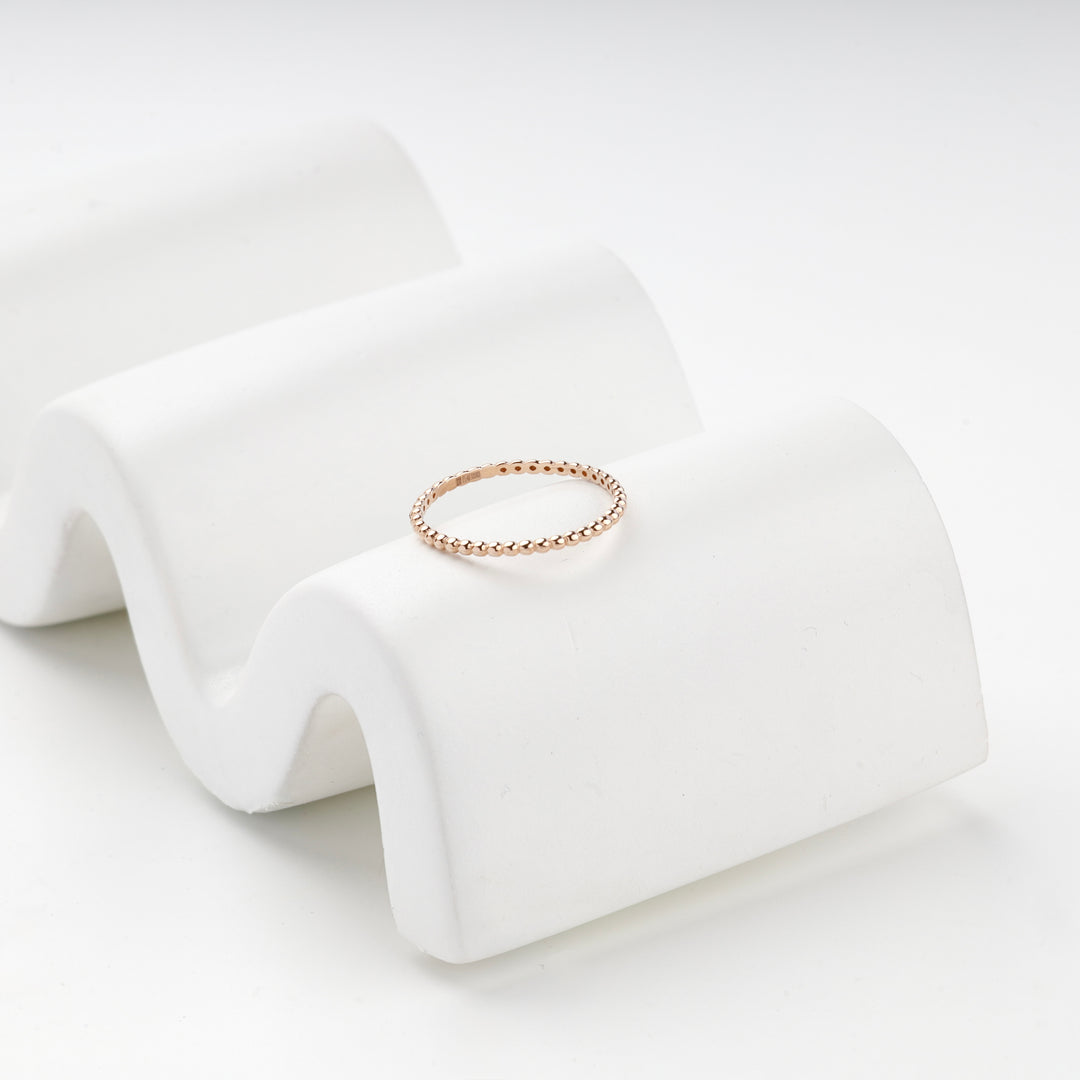Rose gold beaded band ring on a white wave-shaped stand