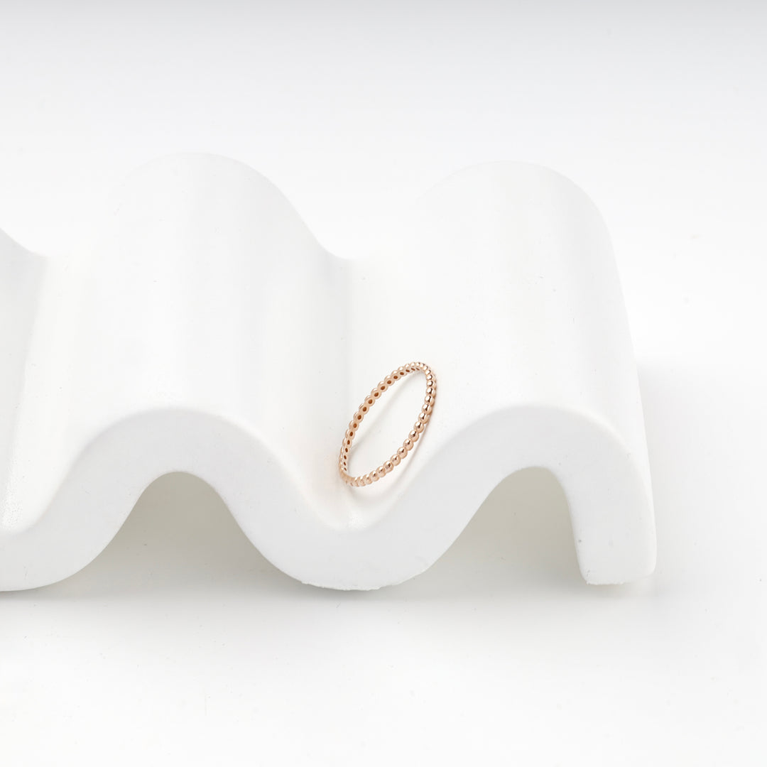 Rose gold beaded band ring resting on a white curved stand, hallmark visible inside