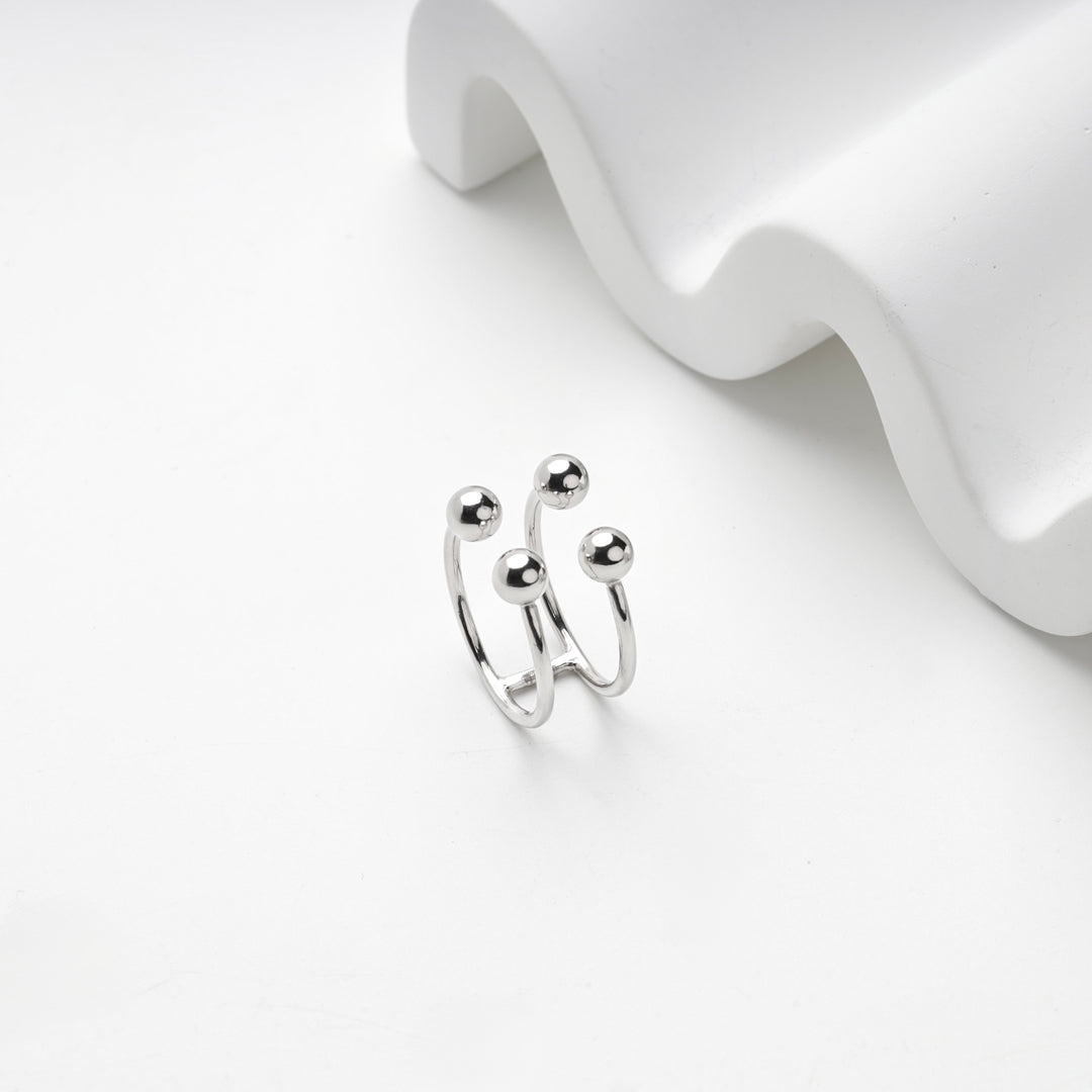 Silver 925 four ball ring standing beside a white wave-shaped display block
