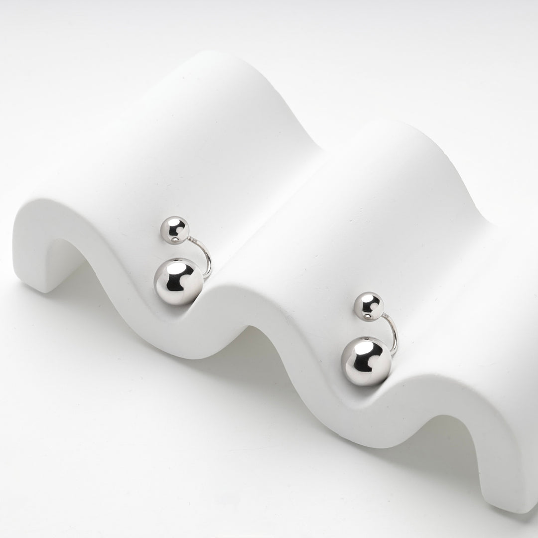 Silver 925 ball duo earrings resting on a white wave stand