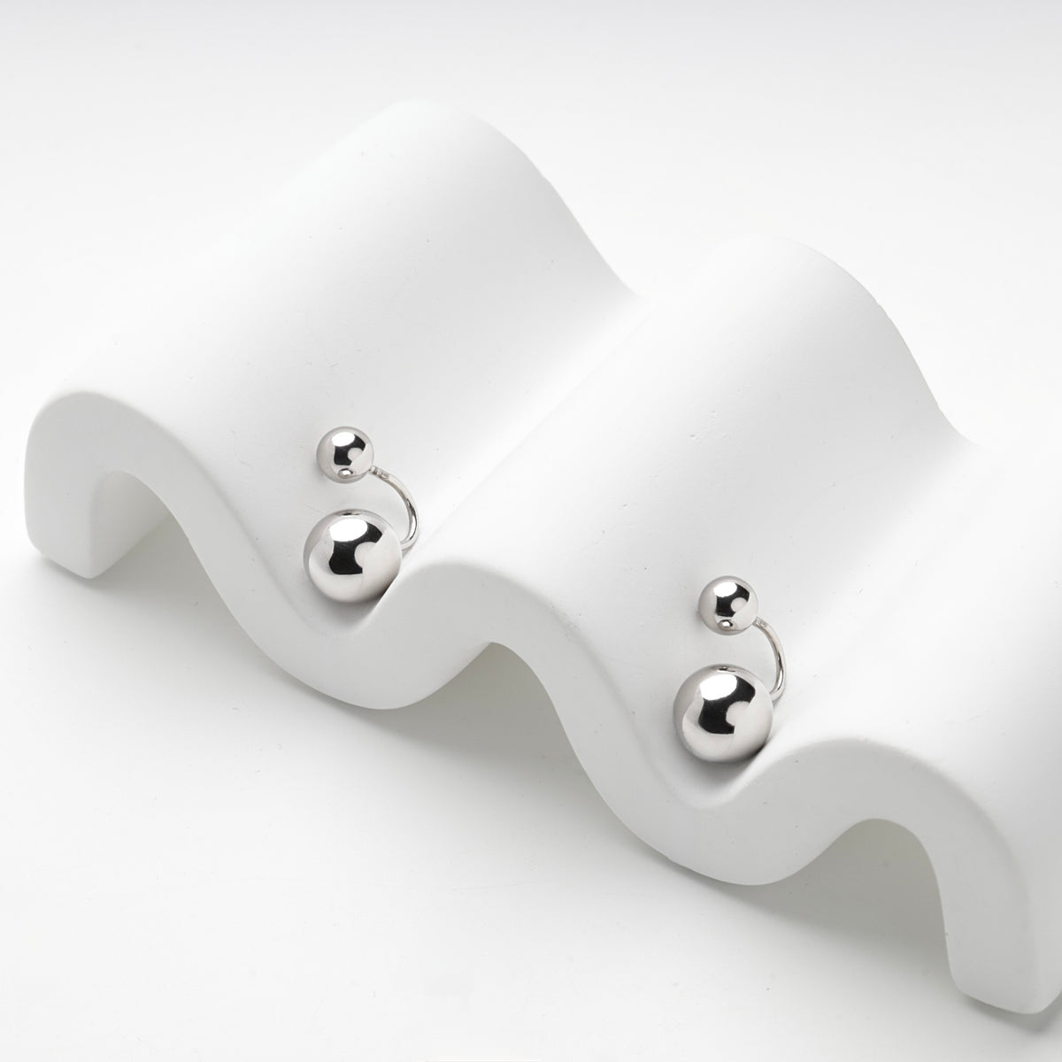 Silver 925 ball duo earrings resting on a white wave stand