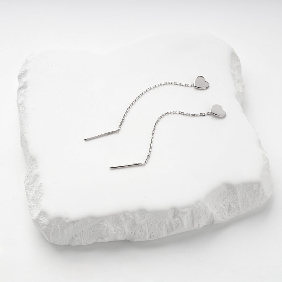 Pair of silver 925 heart threader earrings on a white stone slab